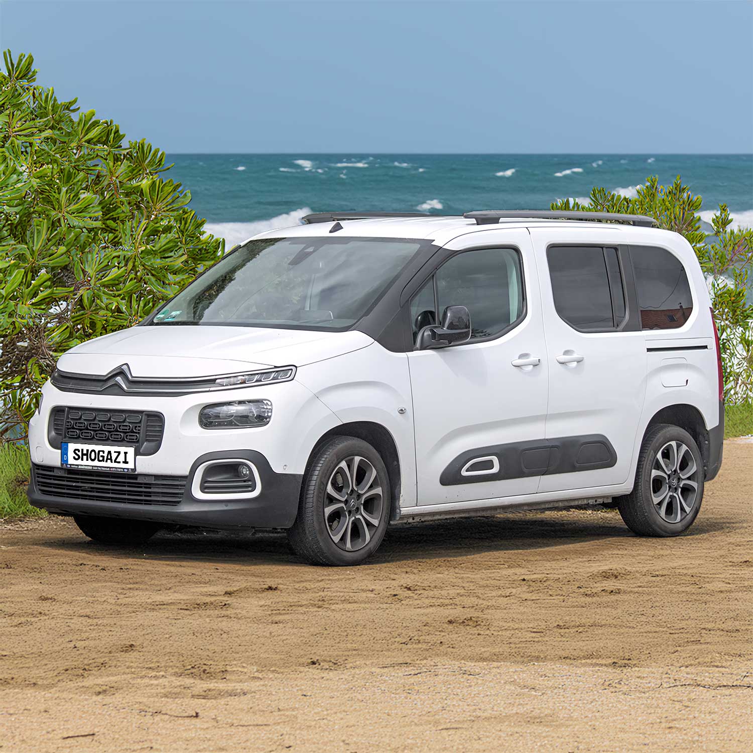 Citroen Berlingo steht im Sand mit Meer, Wellengang und Sträuchern im Hintergrund – Matratze 103x192 cm für komfortables Camping